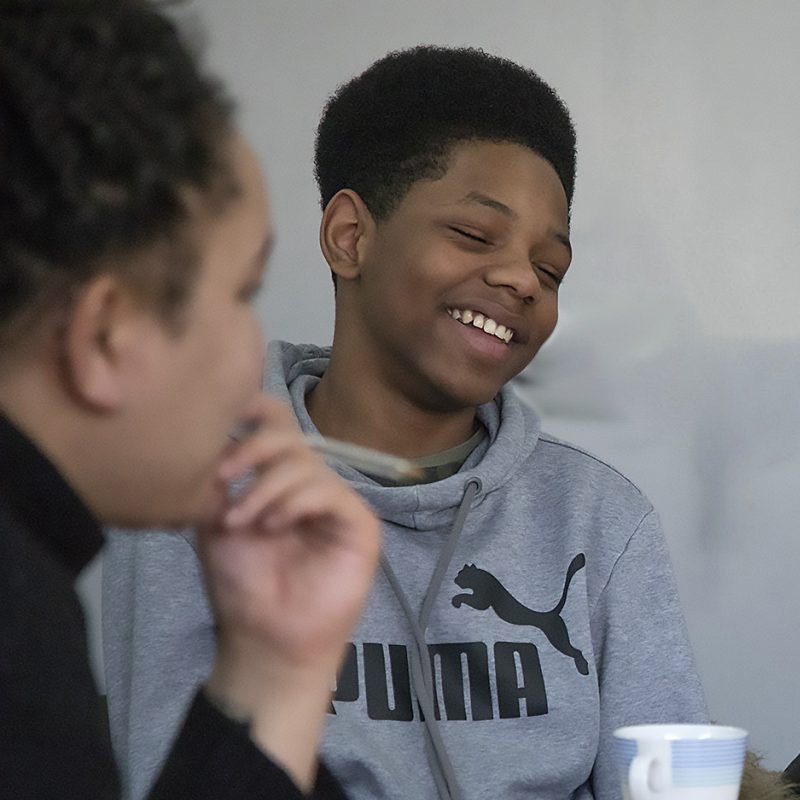 Two people sitting together, one smiling and wearing a gray Puma hoodie, the other with a hand near their chin. | SEN Schools