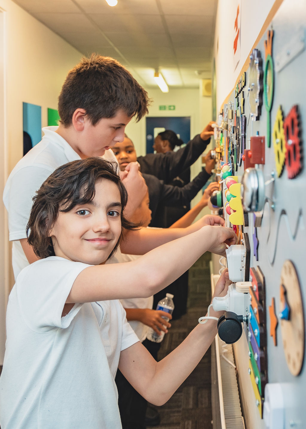 Students engage with a tactile educational board in a school hallway. | SEN Schools